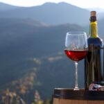 Corkscrew, glass and bottle of red wine on barrel against mountain landscape, space for text