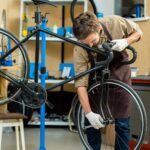 Young master in uniform fixing bolt on wheel of bicycle in workroom